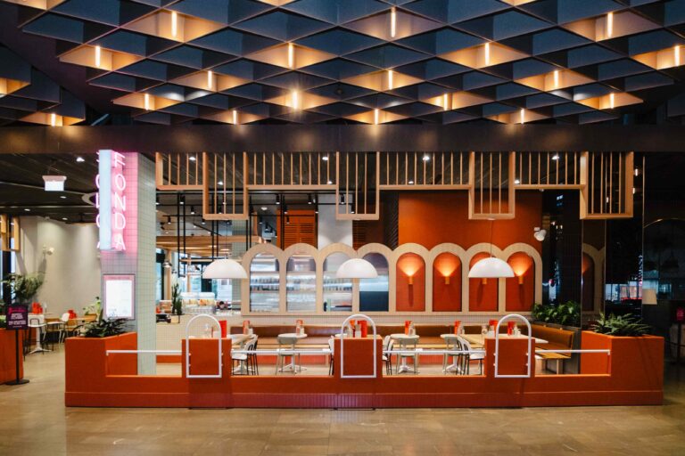 Front view of a stylish restaurant interior shopfitting fitout with a warm color palette, featuring curved red partitions, white round tables, and mixed seating arrangements.