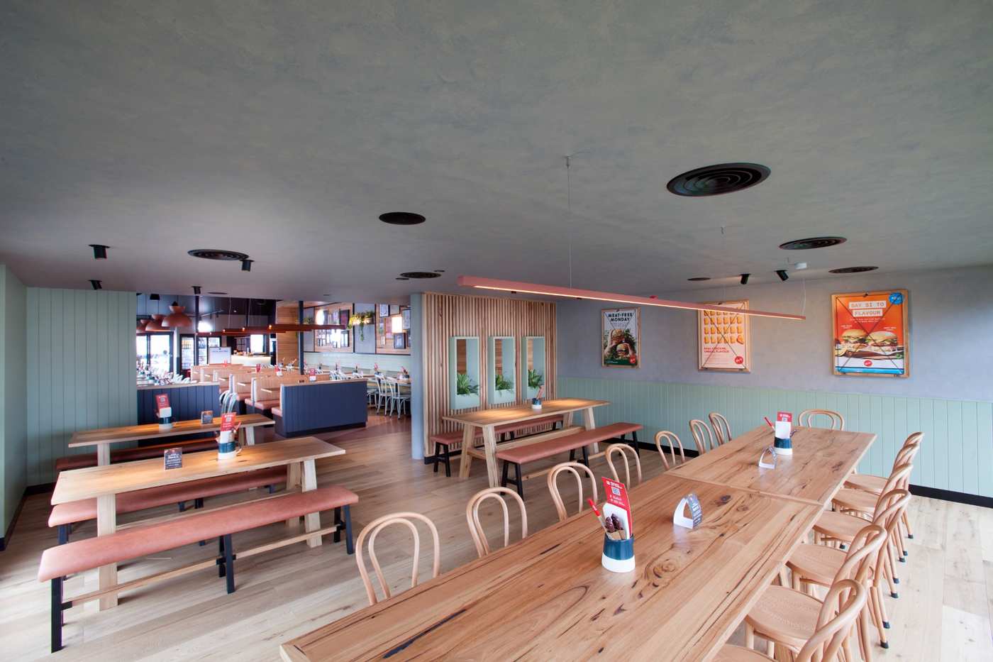 Modern hospitality fit-out at Grill’d Tunstall Square featuring custom timber joinery, communal dining tables, booth seating, feature wall panelling, and integrated restaurant fit-out detailing by Shape Shopfitters.